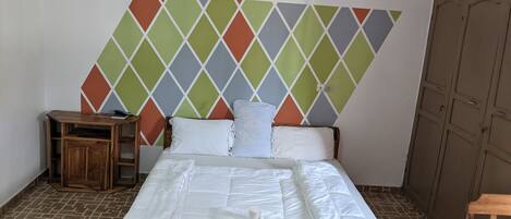 A neatly made bed with white linens, a wooden headboard, and a colorful diamond-patterned wall behind it.