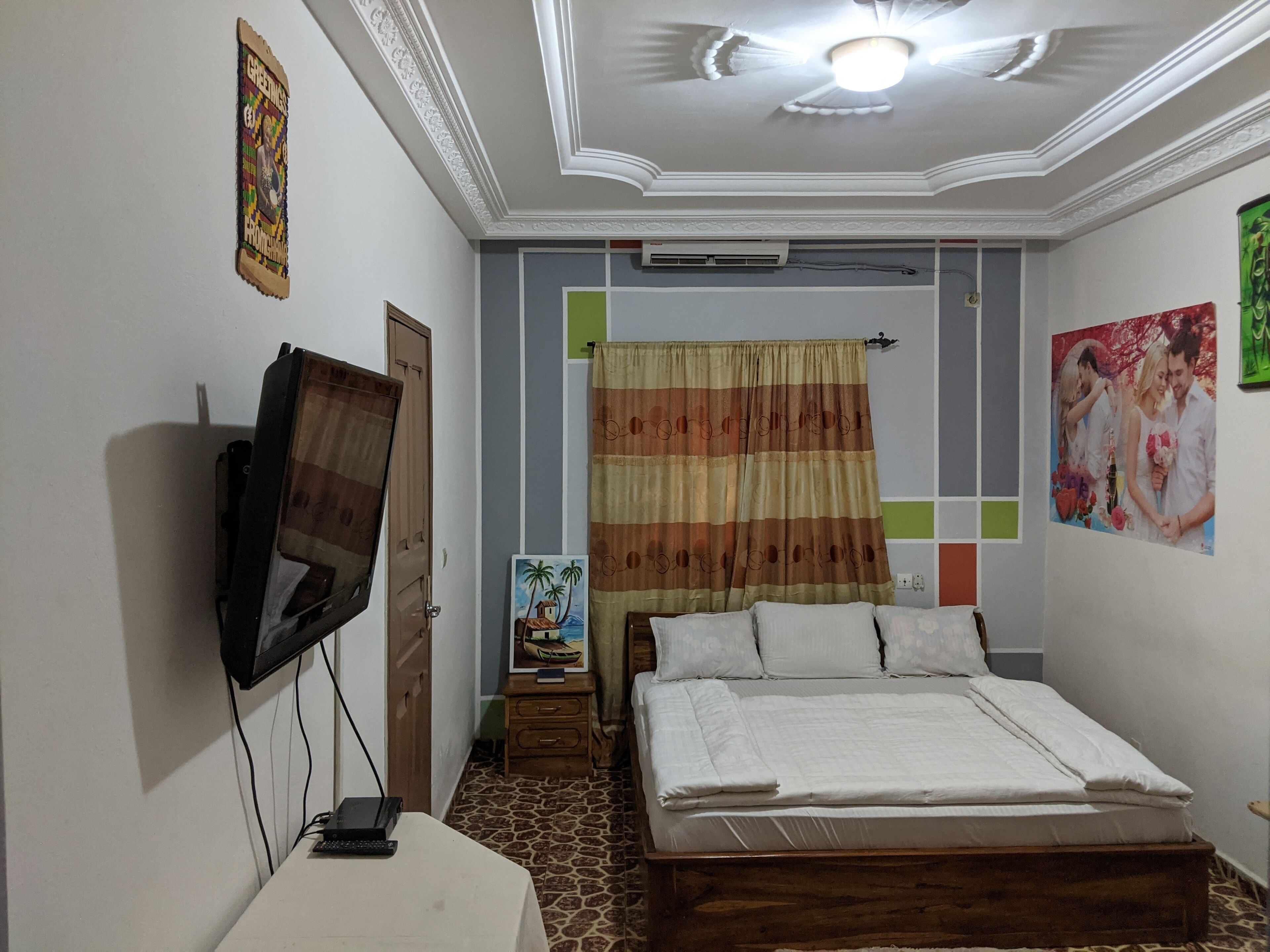 Un dormitorio con cama, televisor montado en la pared, aire acondicionado y un cuadro.