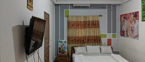 Un dormitorio con cama, televisor montado en la pared, aire acondicionado y un cuadro.