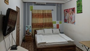 Un dormitorio con cama, televisor sobre un mueble bajo, un cuadro en la pared y un ventilador de techo.