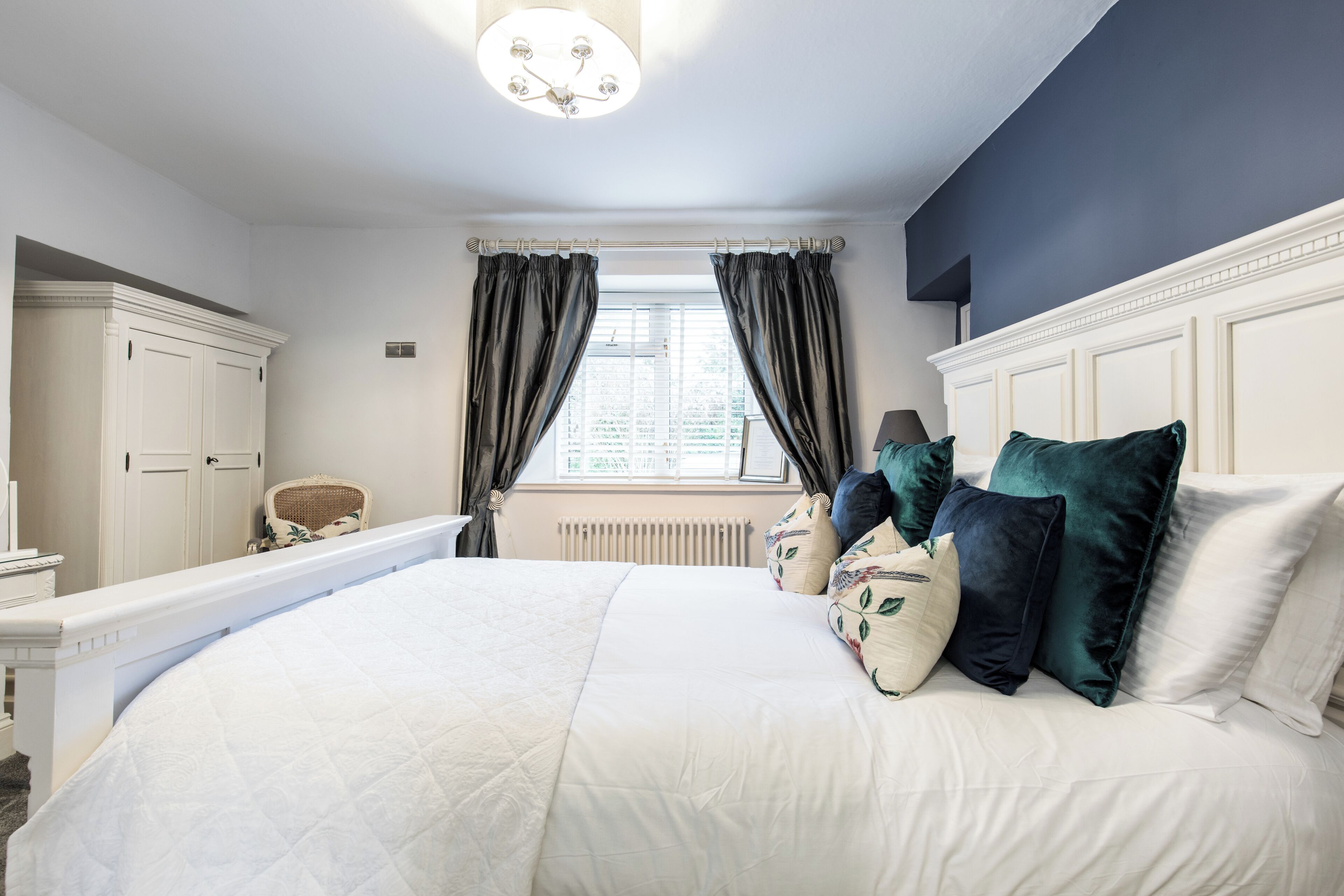 Ein Hotelzimmer mit einem großen Bett, einem Sessel, einem Schreibtisch und einem Fenster mit Vorhängen.