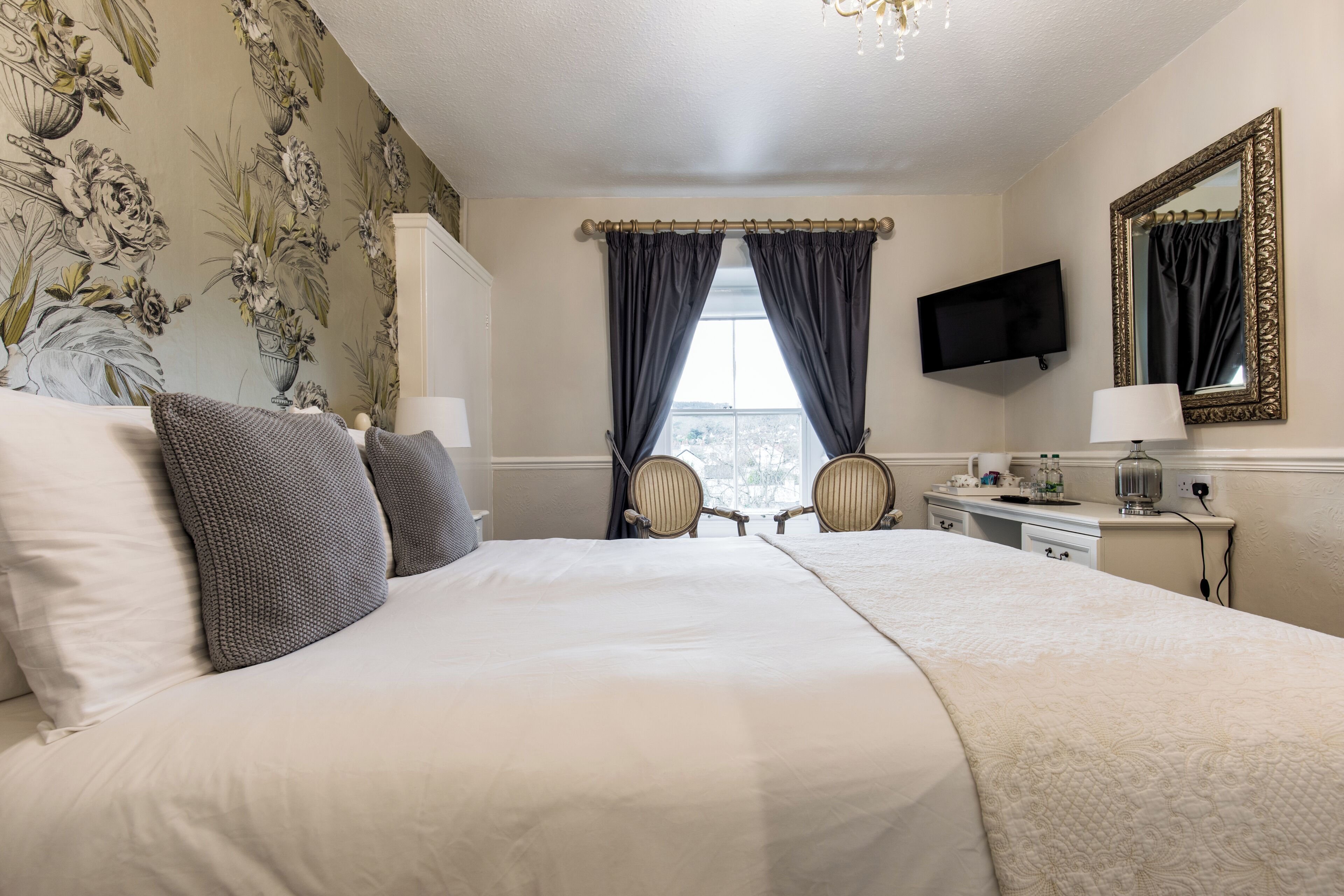 A hotel room with a large bed, two chairs, a desk, a television, and a window with curtains.