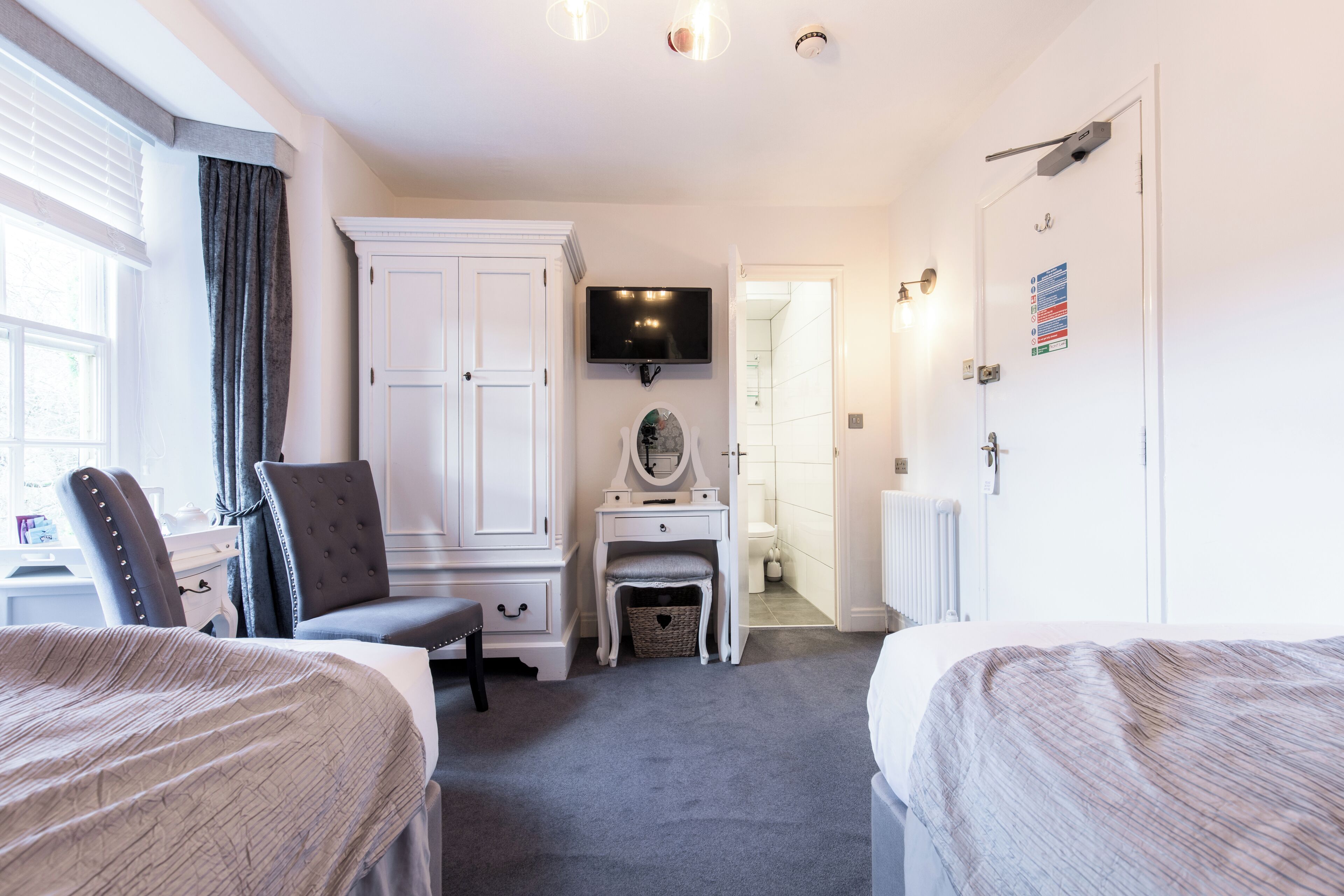 A hotel room with two beds, a vanity with a mirror, a television, and a large white wardrobe.