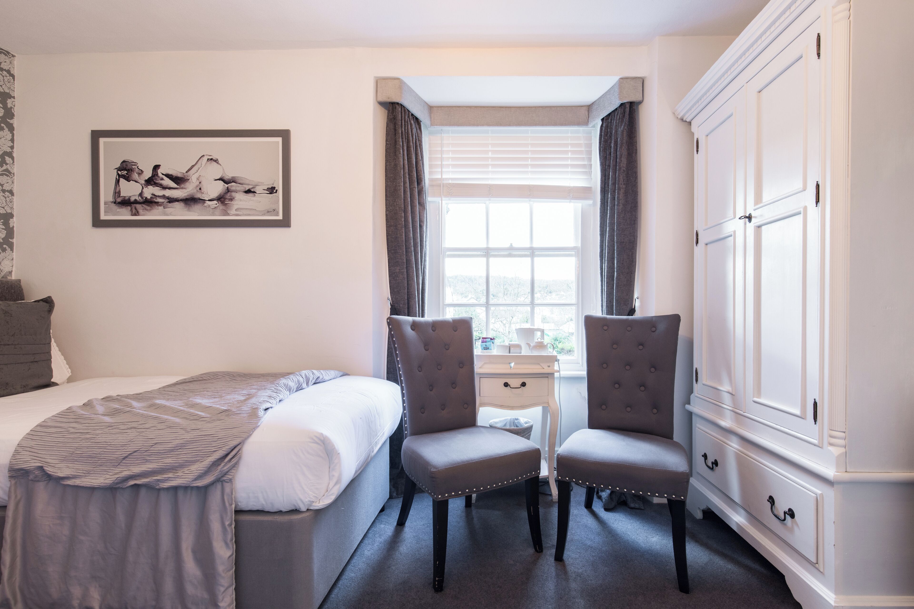 A hotel room with a bed, two chairs, a desk, and a wardrobe.