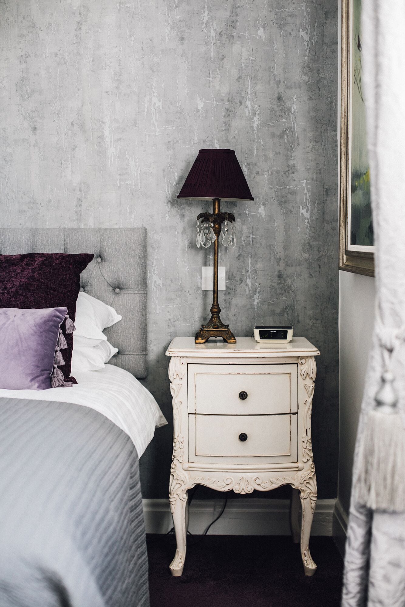 Un dormitorio con una cama, una mesita de noche con lámpara y un reloj de pared.