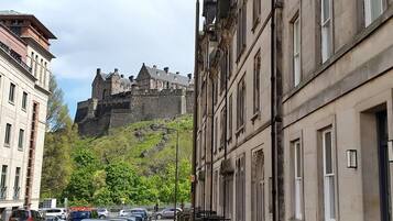 A street with parked cars and a historic building with a castle-like structure in the background.