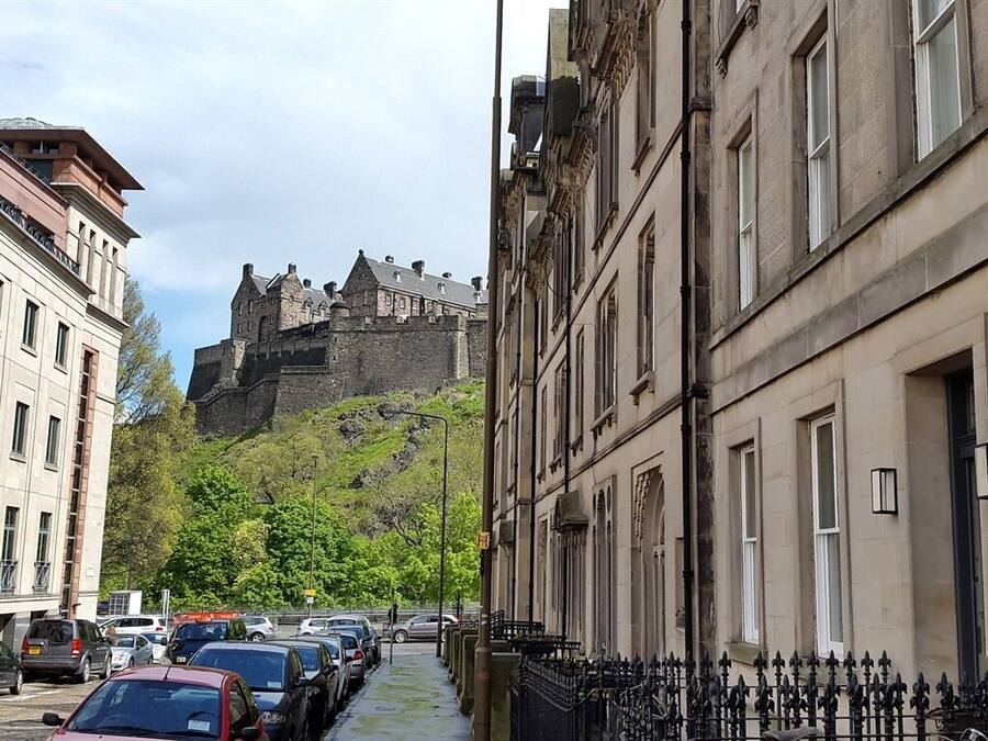 A street with parked cars and a historic building with a castle-like structure in the background.