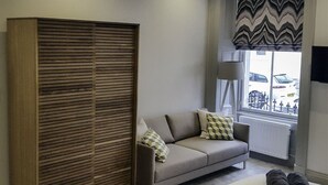 Una habitación moderna con sofá, armario de madera y ventana con vistas a coches aparcados.