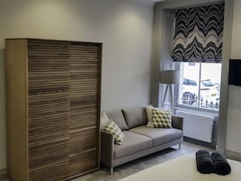 Una habitación moderna con sofá, armario de madera y ventana con vistas a coches aparcados.