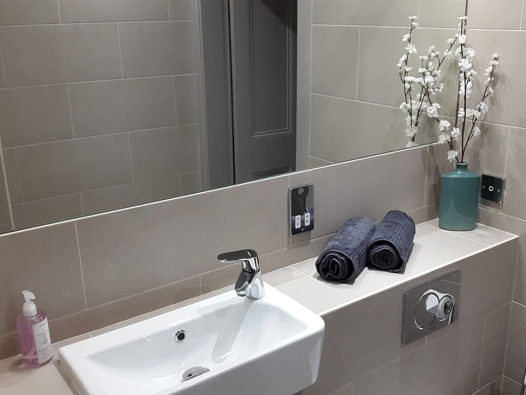 A modern bathroom with a white sink, a mirror, a towel rack, and a vase with flowers.