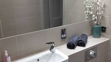 A modern bathroom with a white sink, a mirror, a towel rack, and a vase with flowers.