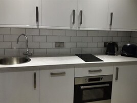A kitchen with white cabinets, a stainless steel sink, a black countertop, and a built-in oven.