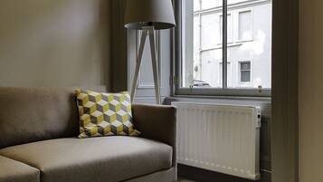 A room with a sofa, a patterned pillow, a floor lamp, and a window with a view of buildings outside.