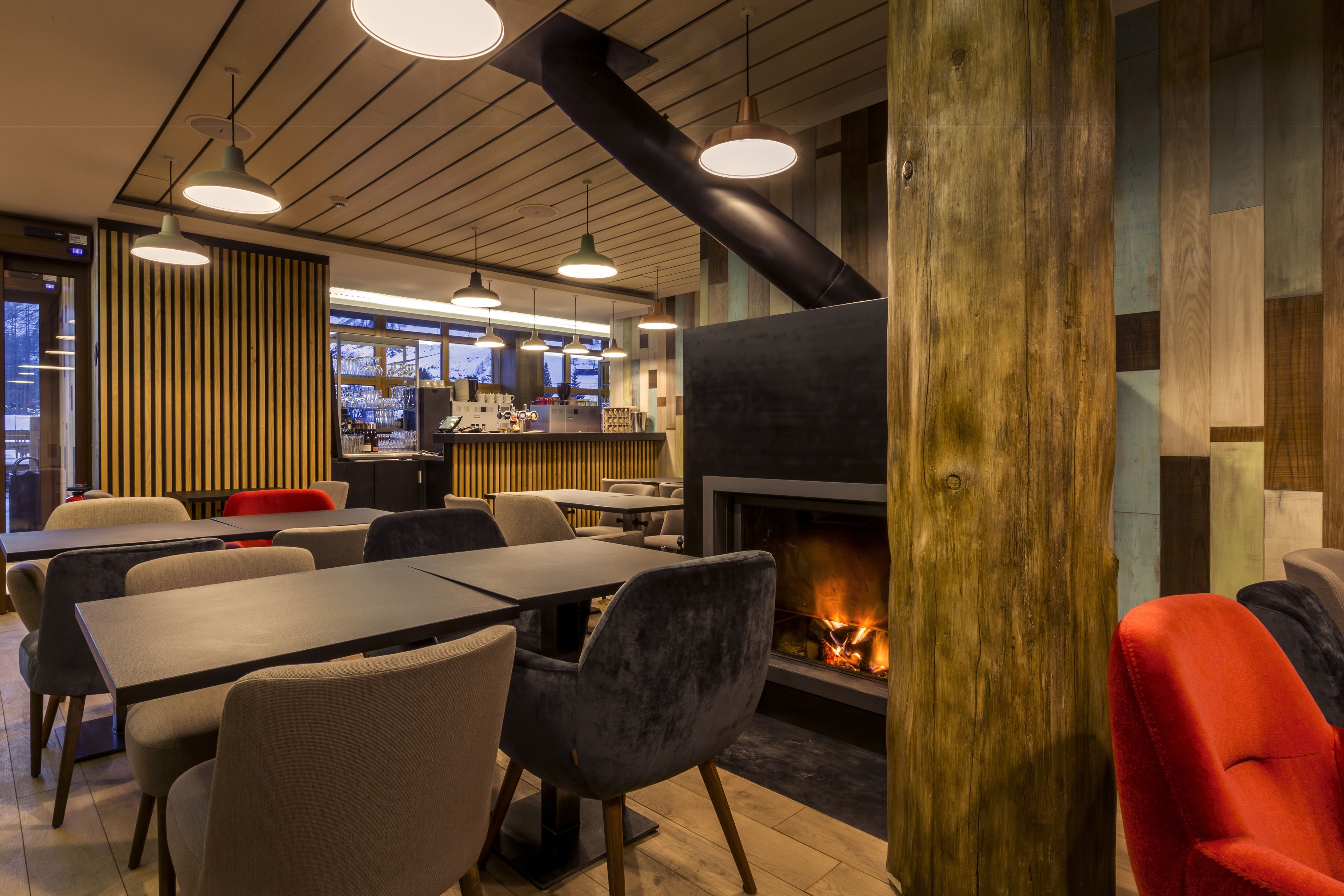 Un intérieur de restaurant moderne, avec une cheminée centrale, des lambris en bois et un mobilier contemporain.
