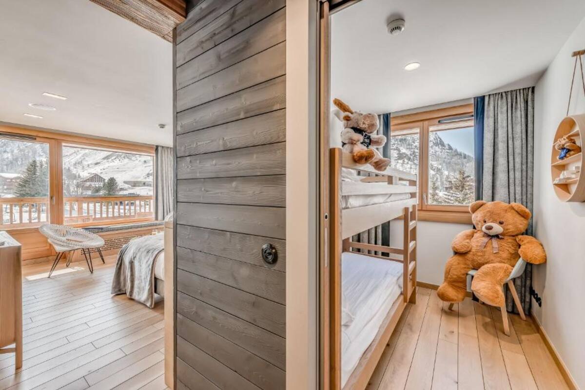 Una habitación acogedora con suelo de madera, literas, un osito de peluche y vistas a montañas nevadas.
