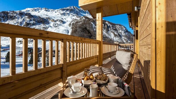 A wooden deck with a breakfast tray, pillows, and a view of snow-covered mountains. - Le Yule Hotel & Spa (Val-d'Isere)