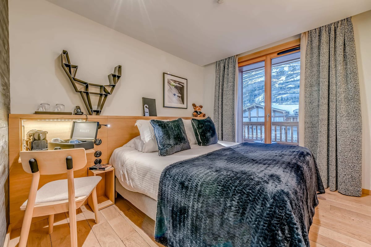 Un dormitorio con una cama grande, un escritorio con una computadora, una silla y una ventana con vista a una montaña.