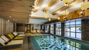 A large indoor swimming pool with a geometric tile pattern, wooden beams, and a seating area with sun loungers. - Le Yule Hotel & Spa (Val-d'Isere)