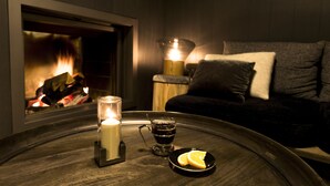 A cozy room with a fireplace, a candle, a glass of dark liquid, and a plate with slices of orange. - Le Yule Hotel & Spa (Val-d'Isere)