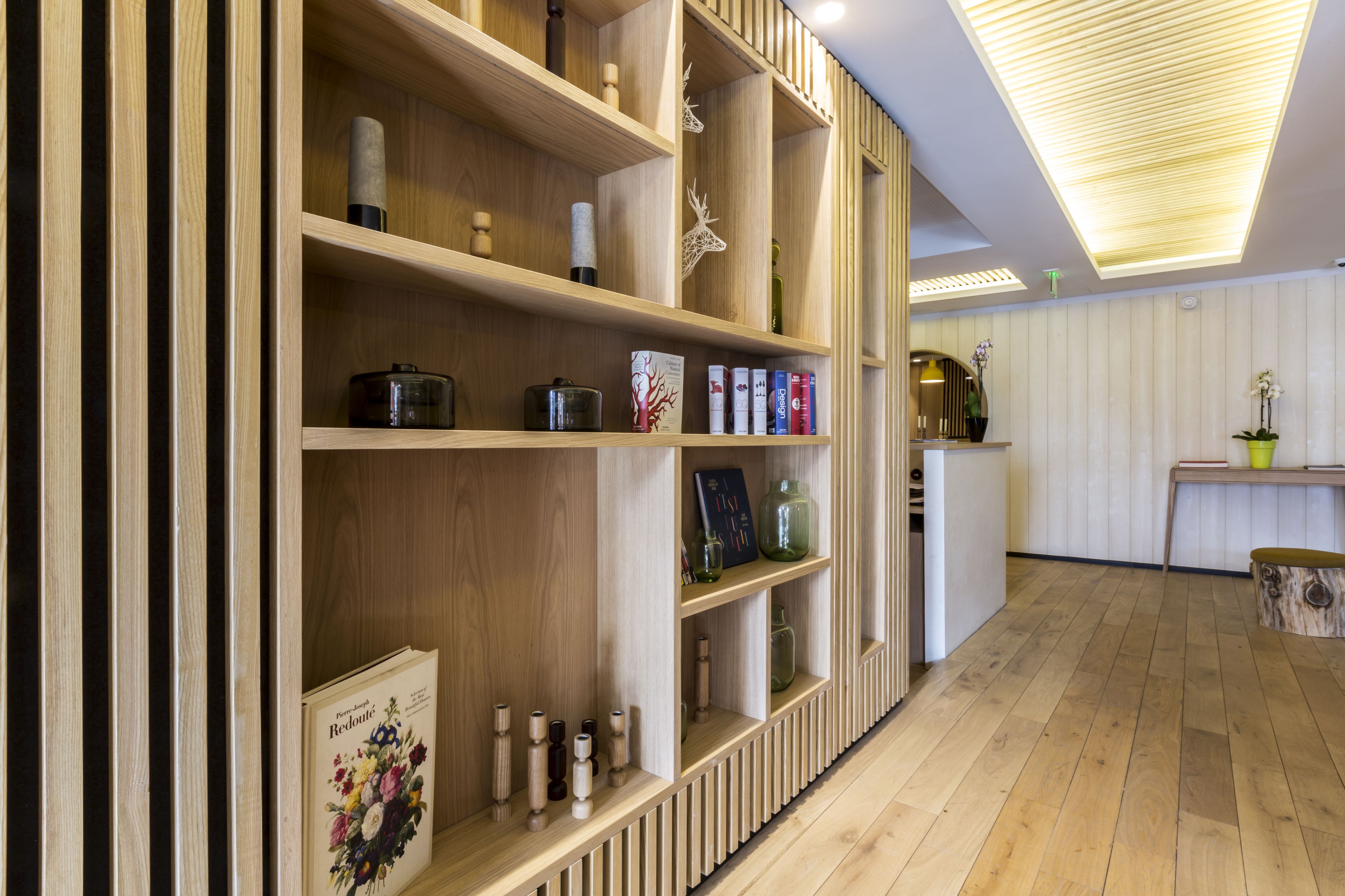 Un interior moderno con estanterías de madera que exhiben diversos objetos, suelo de madera e iluminación lineal en el techo.