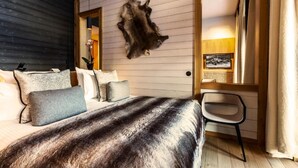 A bedroom with a large bed, a mounted fur rug, a chair, and a wooden door leading to another room. - Le Yule Hotel & Spa (Val-d'Isere)