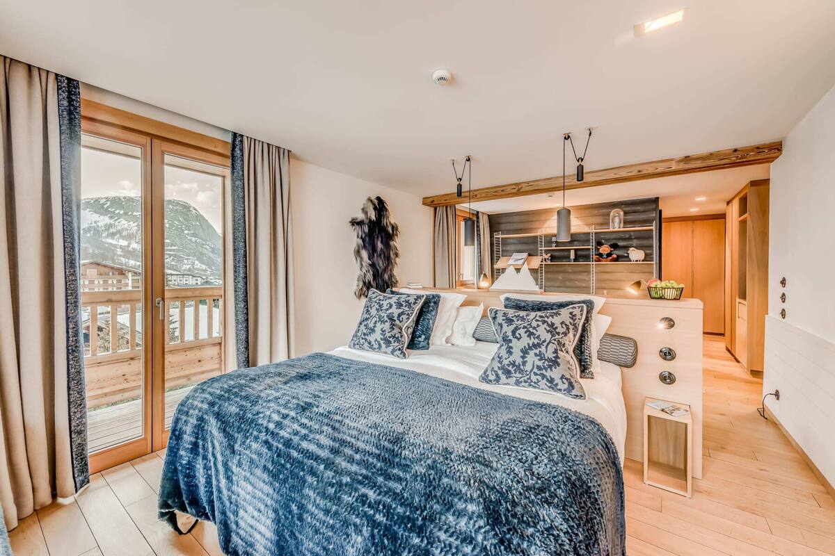 Un dormitorio con una cama grande, techo de madera, armario empotrado y balcón con vistas a las montañas.
