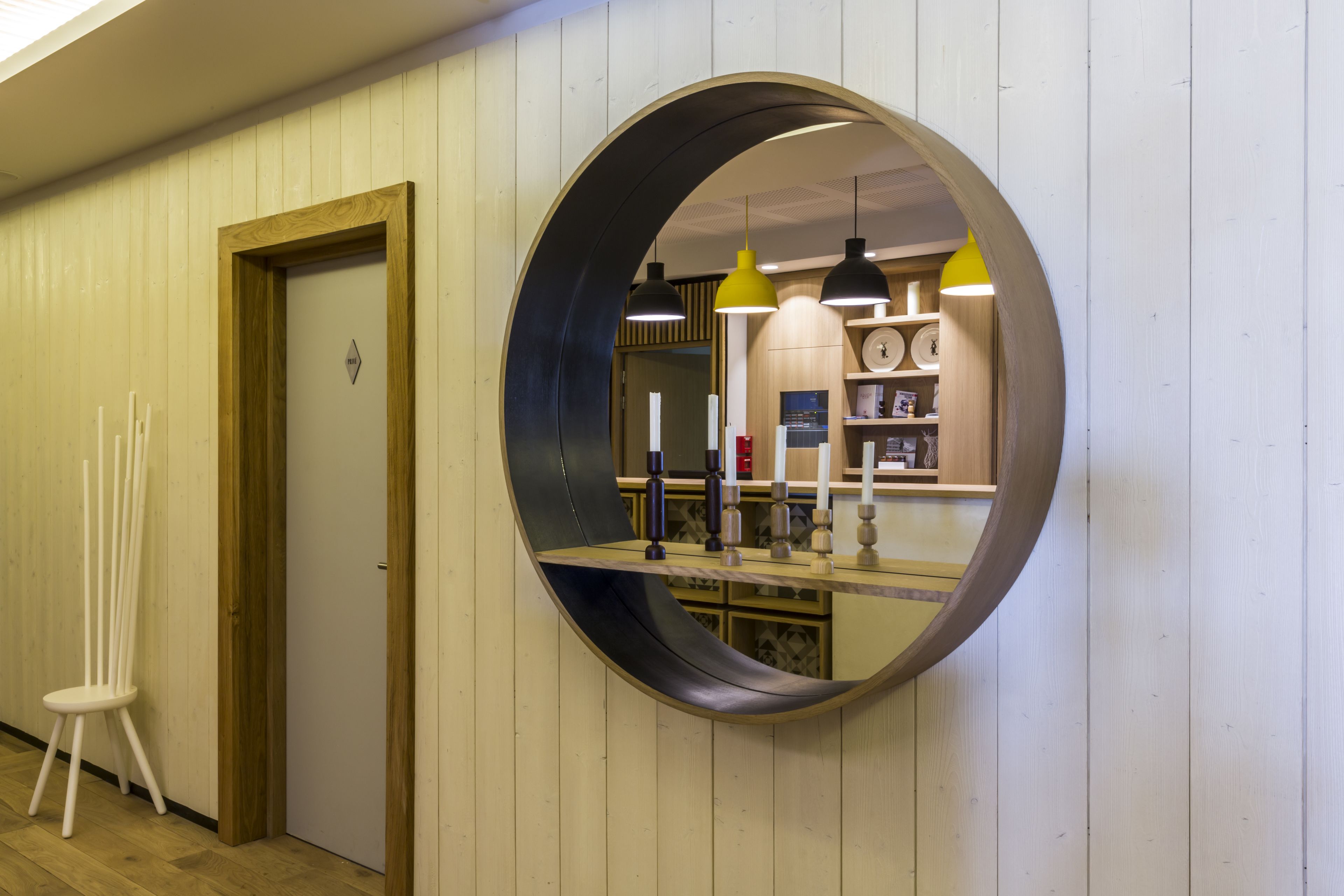 A circular mirror on a wall with a wooden door and a white chair to the left.