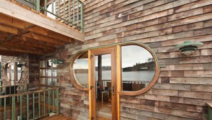 Una baita di legno con veranda, una finestra circolare e vista su un lago.