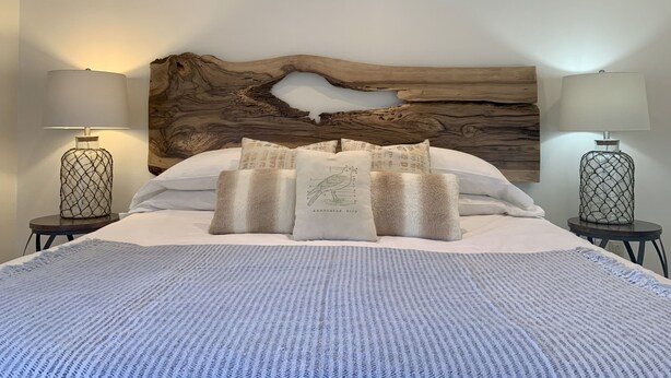 A bedroom with a large bed, two bedside tables with lamps, a wooden headboard, and a textured blanket.