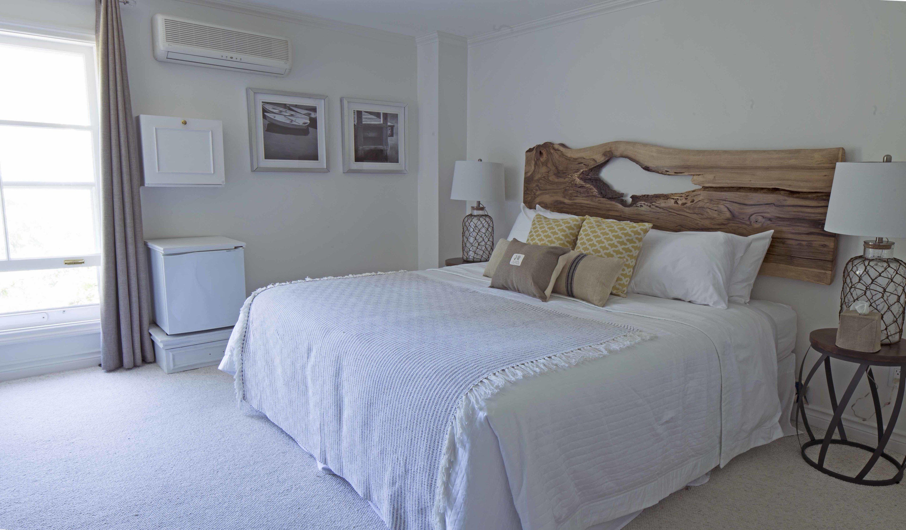 Une chambre à coucher avec un grand lit, une tête de lit en bois, une table de chevet avec une lampe et une fenêtre avec des rideaux.