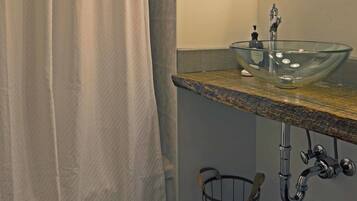 A bathroom with a glass sink, a shower curtain, a mirror, and a pebbled floor.