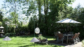 A patio with a table and chairs, surrounded by a grassy area and trees.