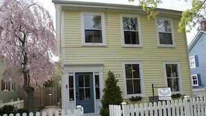 A two-story yellow building with a blue door, white picket fence, and a sign indicating no vacancy.