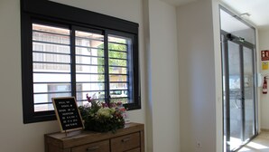 A reception area with a wooden cabinet, a blackboard with text, and a window with blinds. - Hotel Sagunto (Sagunto)