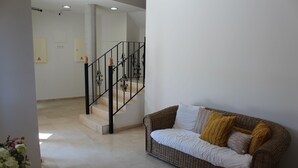 A modern living room with a wicker sofa, a staircase with black railings, and a white wall with a door. - Hotel Sagunto (Sagunto)