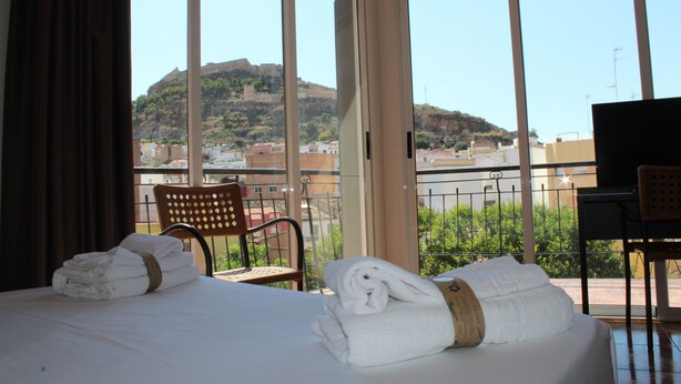 A hotel room with a bed, a chair, a desk, and a view of a hill. - Hotel Sagunto (Sagunto)