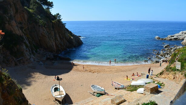 A beach with boats, a rocky cliff, and the sea. - Apartamento Puerto Rico 39 (Tossa de Mar)