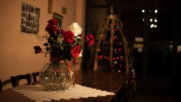 A dining table with a lace tablecloth, a vase with red and white roses, and a Christmas tree in the background.