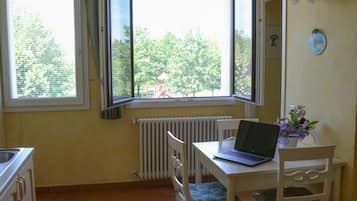 Una pequeña cocina con una mesa y sillas, un ventanal con cortinas y un radiador.