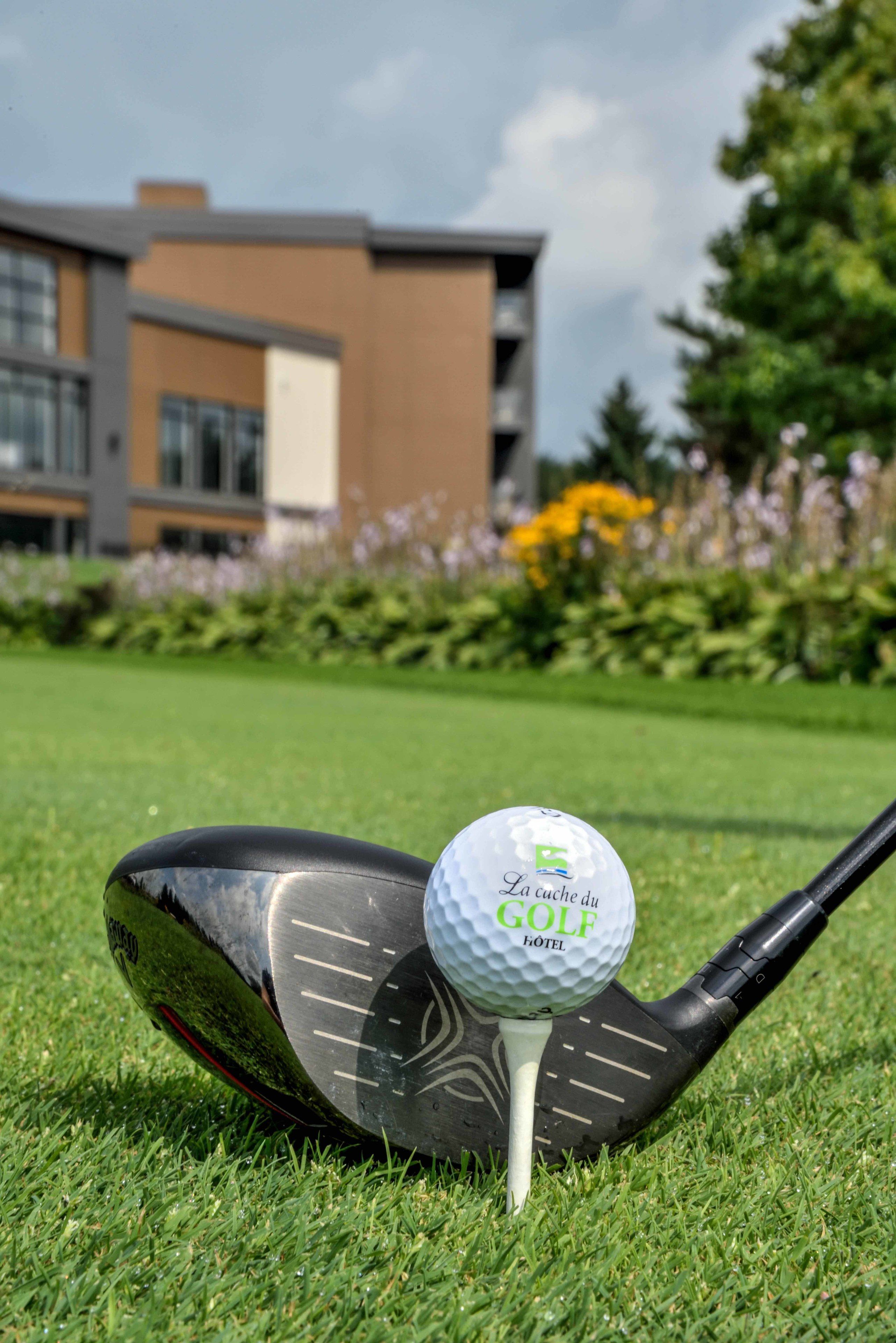 A golf ball on a tee on a green with a modern building in the background.