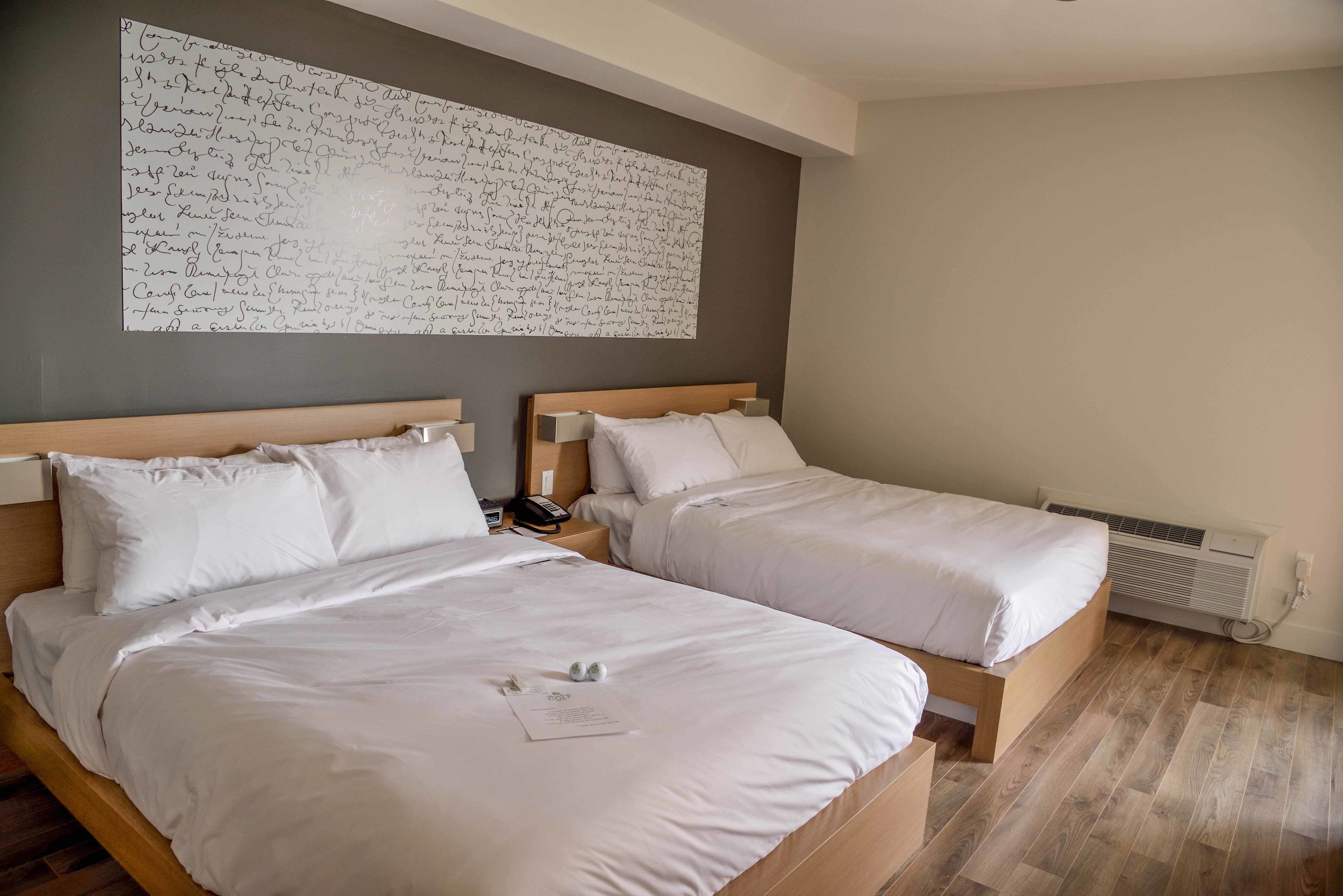 Ein Hotelzimmer mit zwei Betten, einer großen Wand voller handgeschriebener Notizen, einem Nachttisch mit Telefon und einem Heizkörper.