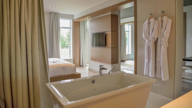 Une chambre d’hôtel moderne dotée d’une grande baignoire, d’un lit, d’une télévision et d’un balcon avec vue.