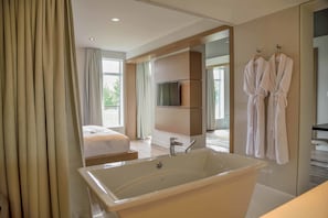 Une chambre d’hôtel moderne dotée d’une grande baignoire, d’un lit, d’une télévision et d’un balcon avec vue.