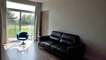 Una sala de estar moderna con un sofá de cuero negro, un sillón azul y un amplio ventanal corredera que da a un balcón.