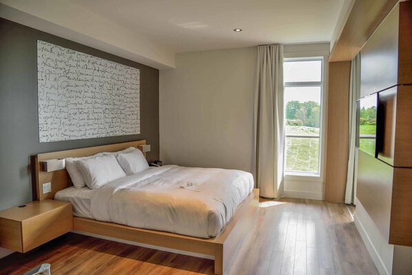 Un dormitorio moderno con una cama grande, una mesita de noche, un televisor montado en la pared y un ventanal con vistas a zonas verdes.