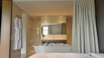 Une chambre d’hôtel moderne dotée d’un grand lit, d’une salle de bain avec baignoire, douche et lavabo avec miroir.