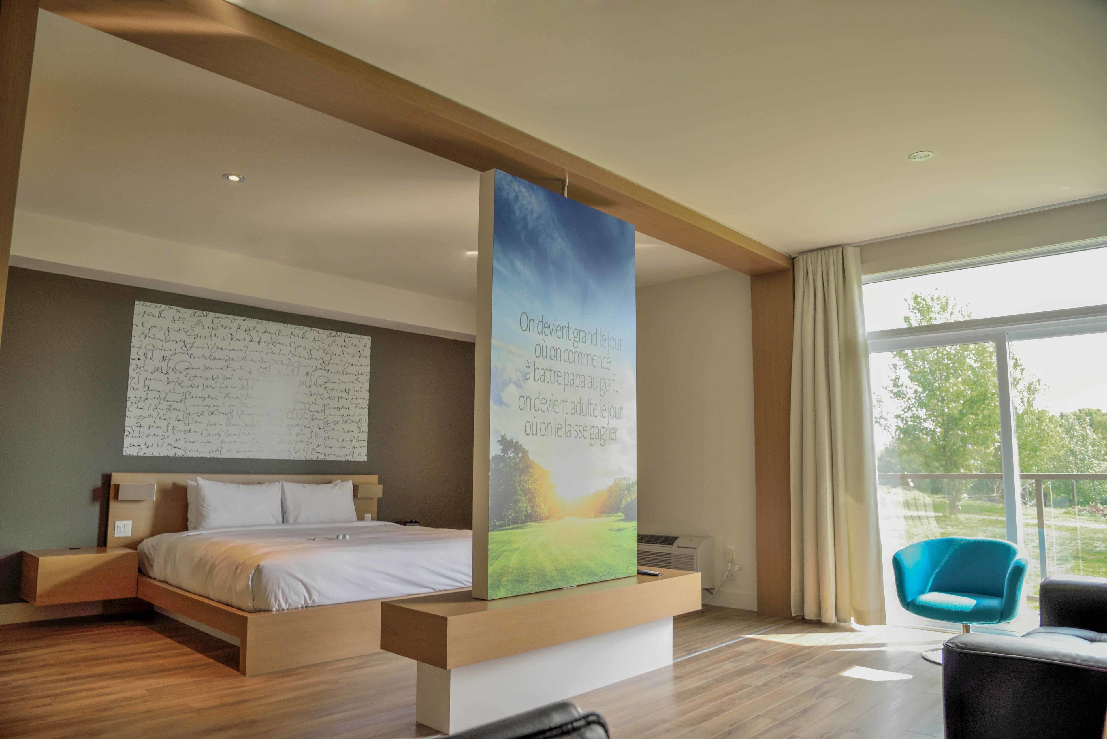 Una habitación de hotel moderna con una cama grande, un escritorio, una silla y un ventanal amplio.