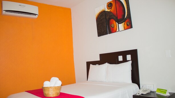 Habitación de hotel con cama, cesta de toallas, mesita de noche con teléfono y equipo de aire acondicionado en la pared.