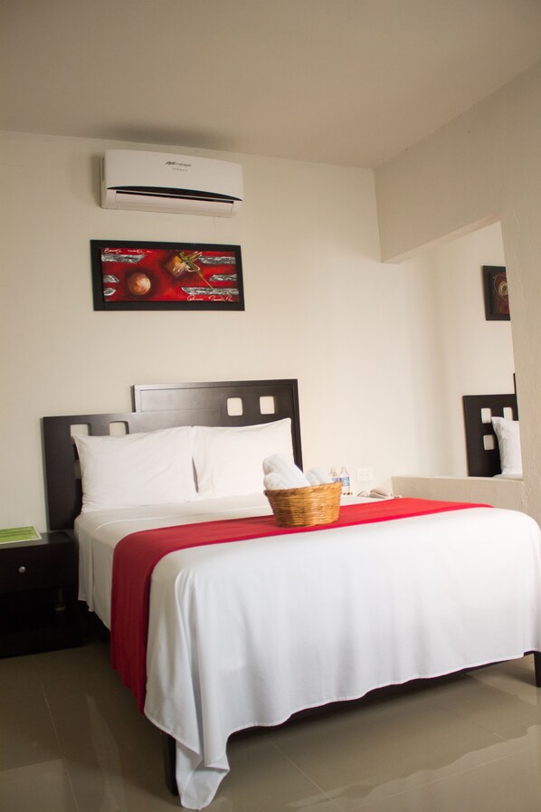 A hotel room with a bed, a nightstand, a wall-mounted air conditioner, and a framed picture above the bed.