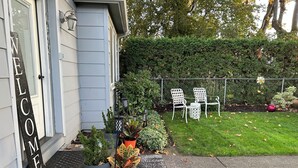 A house with a 'WELCOME' sign, a small garden with potted plants, a lawn, and two white chairs. - Kalmia Cottage (Junction City)